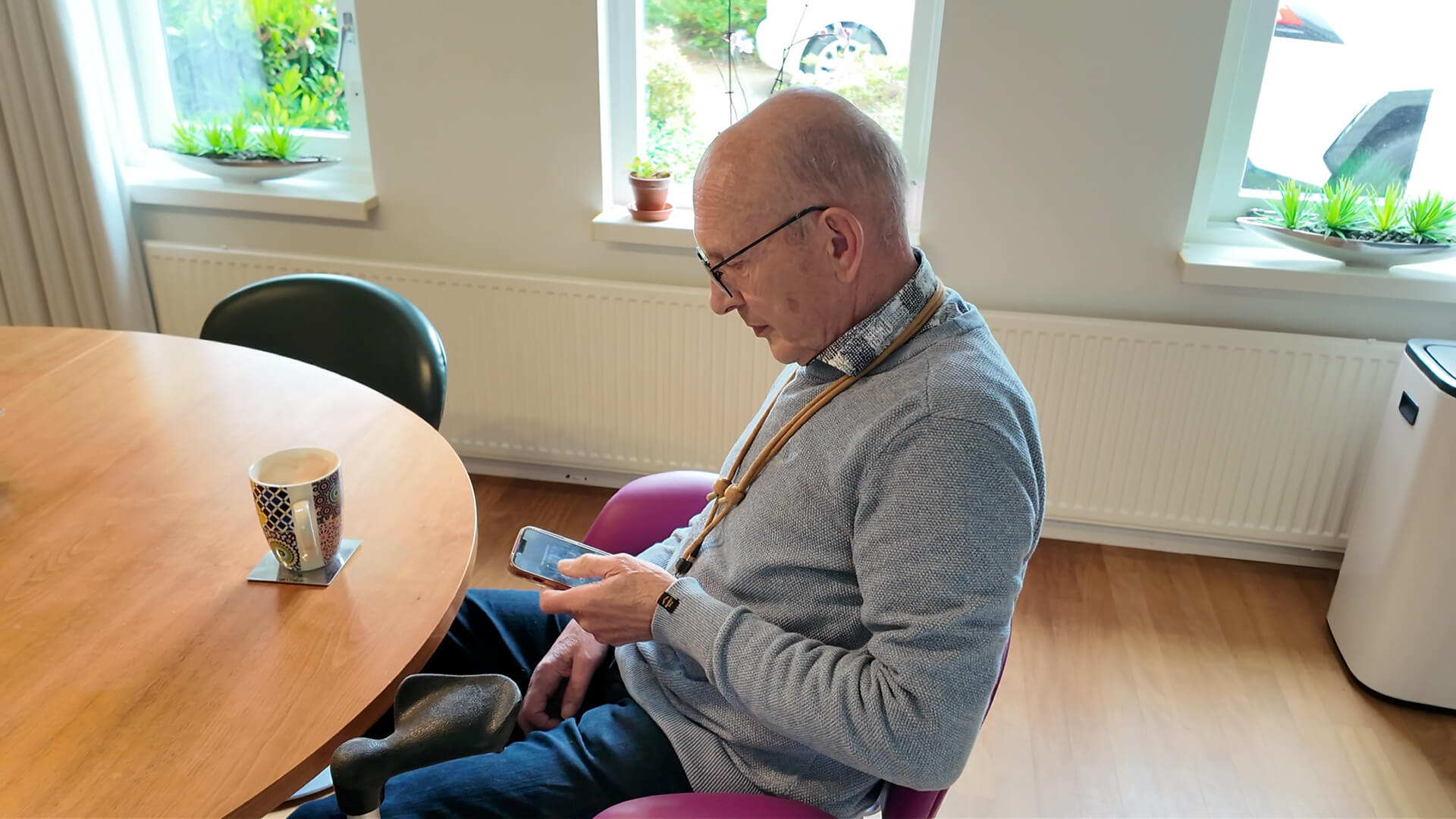 Peter sits at his dining table with a coffee, using the Homey app on his phone