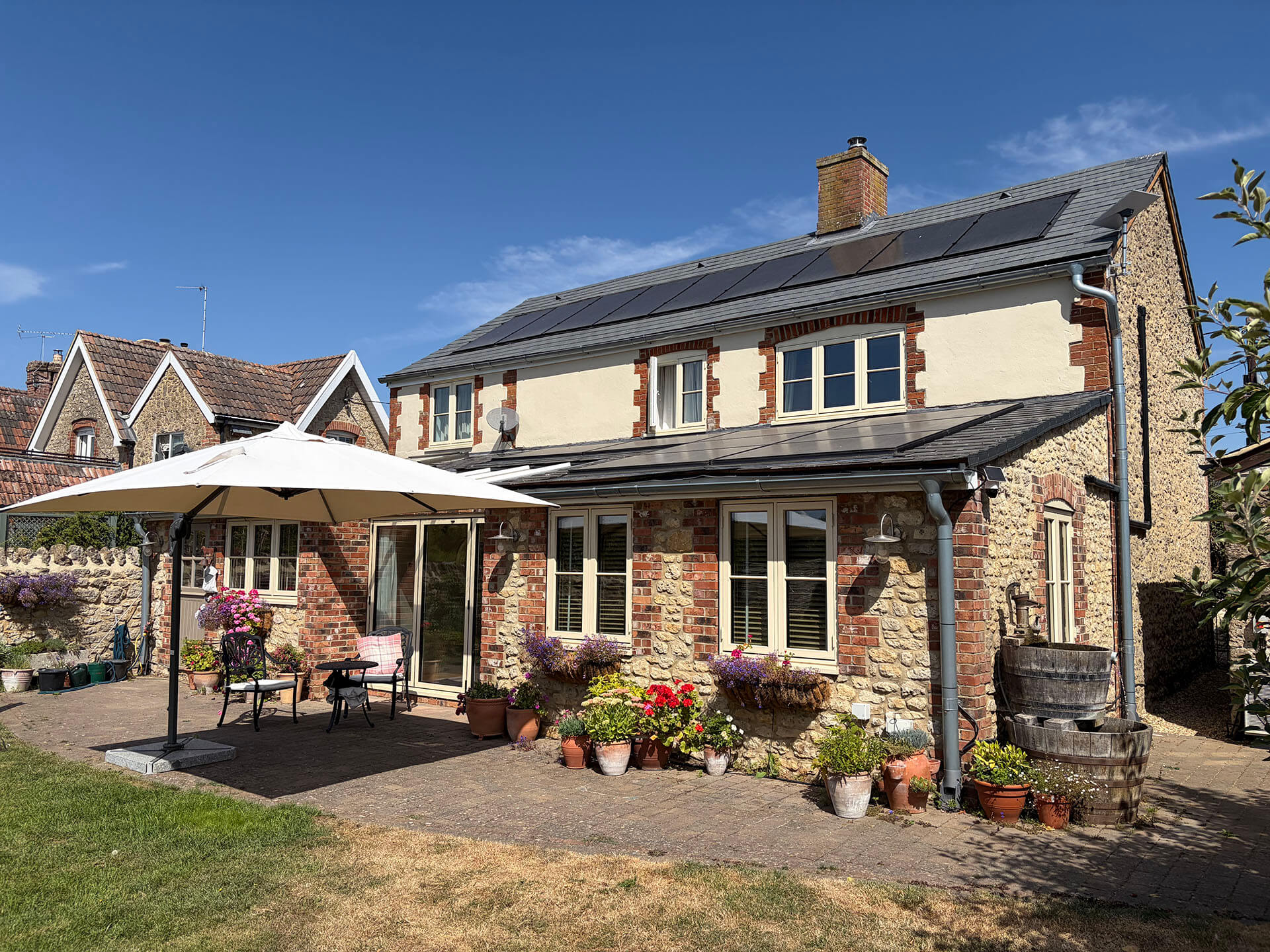 Stone and brick cottage with solar panels across the main roof and rear extension, patio with garden furniture in the foreground.